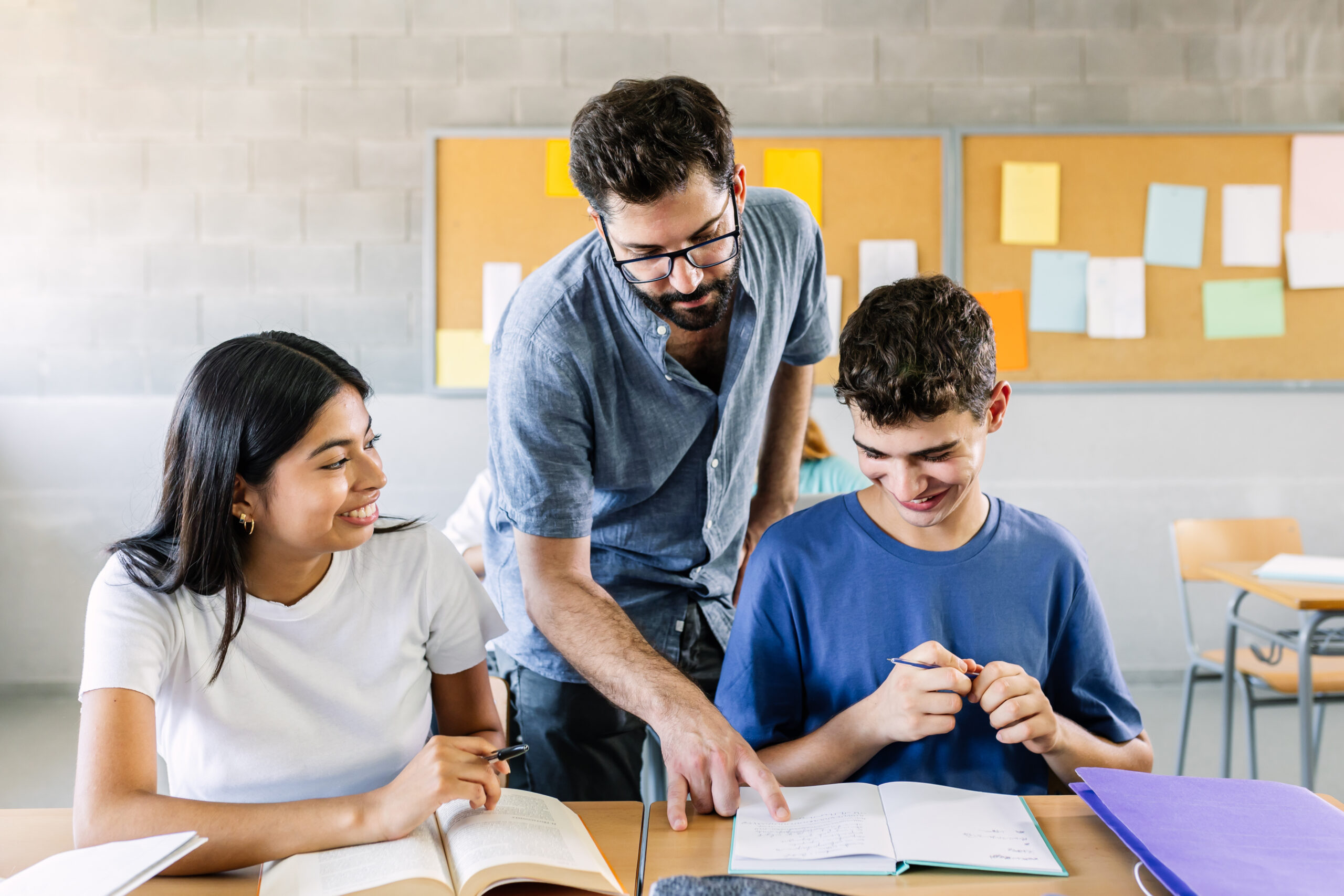 Male teacher helping high school students doing exercises in classroom - Education and college people concept